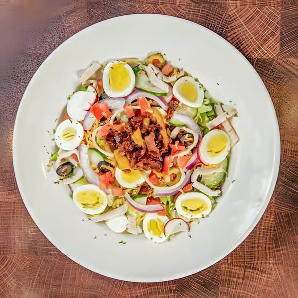A vibrant Nancy's Kitchen diner salad with hard-boiled eggs, bacon, and fresh vegetables on a white plate.