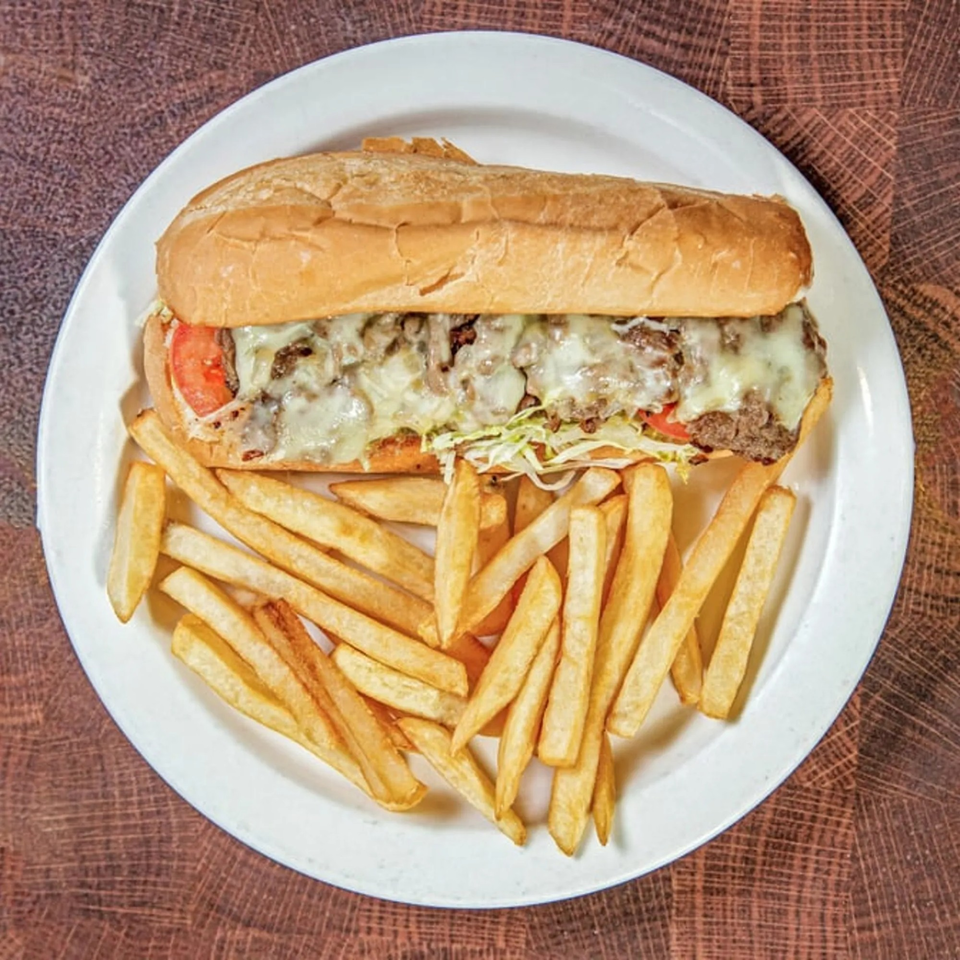 Cheesesteak sandwich with melted cheese, tomatoes, and shredded lettuce, served with golden fries.
