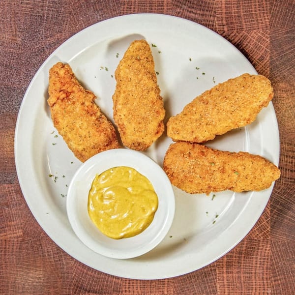 Four crispy chicken tenders with a side of honey mustard dipping sauce on a white plate.