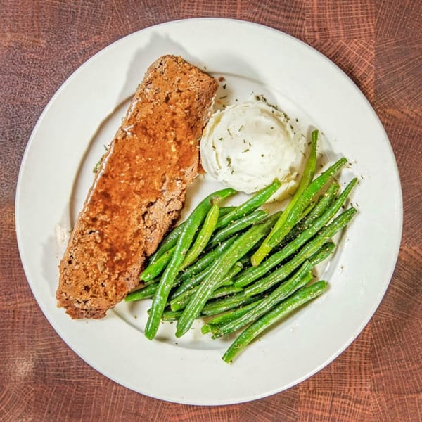 Meatloaf with gravy, mashed potatoes, and green beans on a white plate at Nancy's Kitchen.