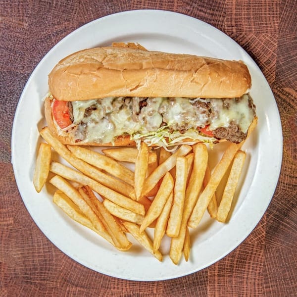A Nancy's Kitchen cheesesteak with melted cheese, tomatoes, and shredded lettuce, served with fries.