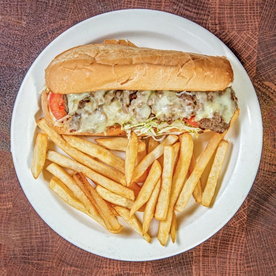 A Nancy's Kitchen cheesesteak with melted cheese, tomatoes, and shredded lettuce, served with fries.