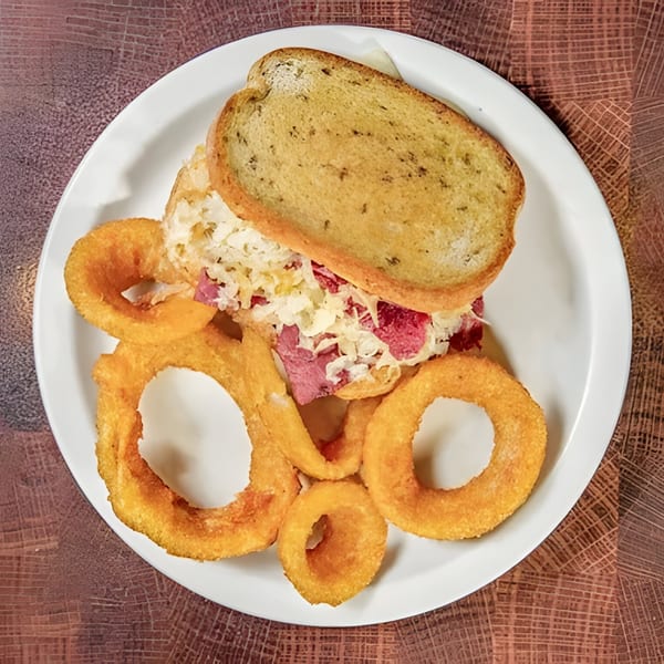 Nancy's Kitchen Reuben sandwich with corned beef, sauerkraut, and onion rings on a white plate.