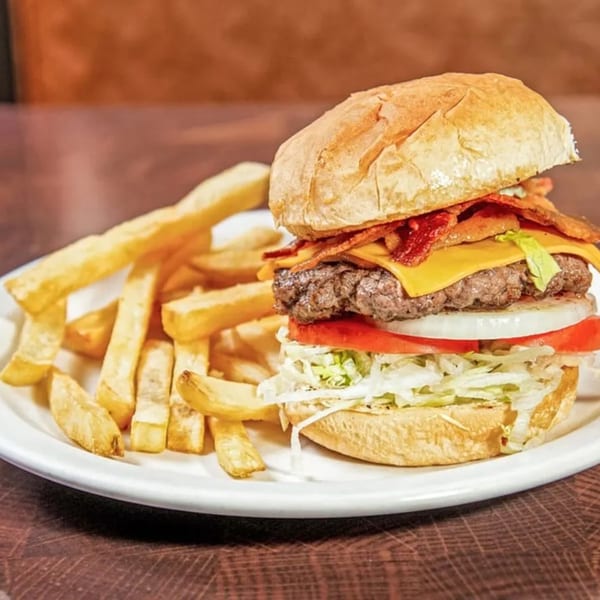 A Nancy's Kitchen bacon cheeseburger with lettuce, tomato, onion, and a side of fries.