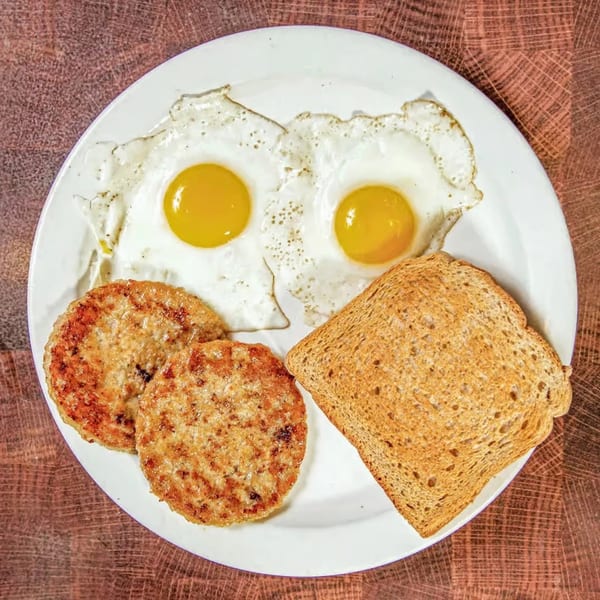 A diner breakfast with two fried eggs, two sausage patties, and a slice of toast on a white plate.