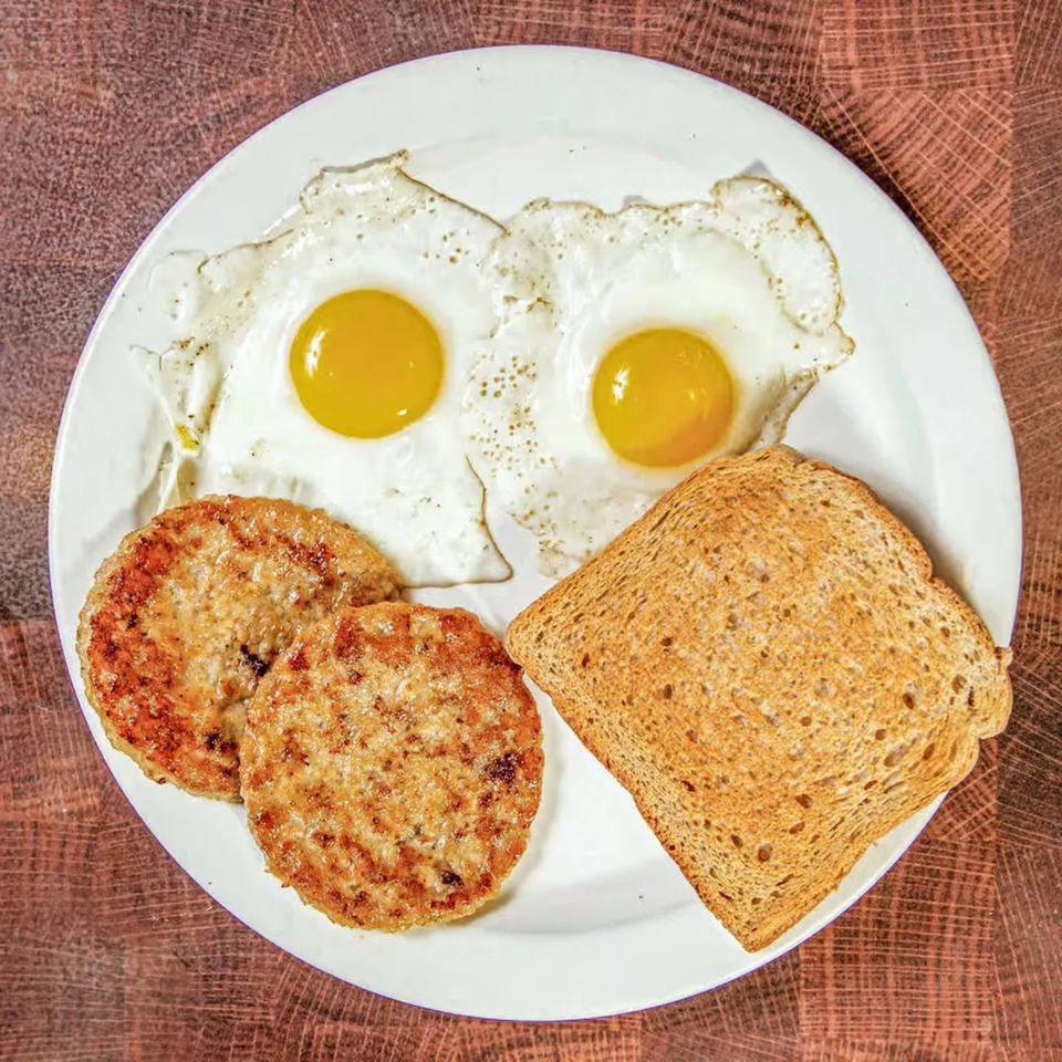 A diner breakfast with two fried eggs, two sausage patties, and a slice of toast on a white plate.